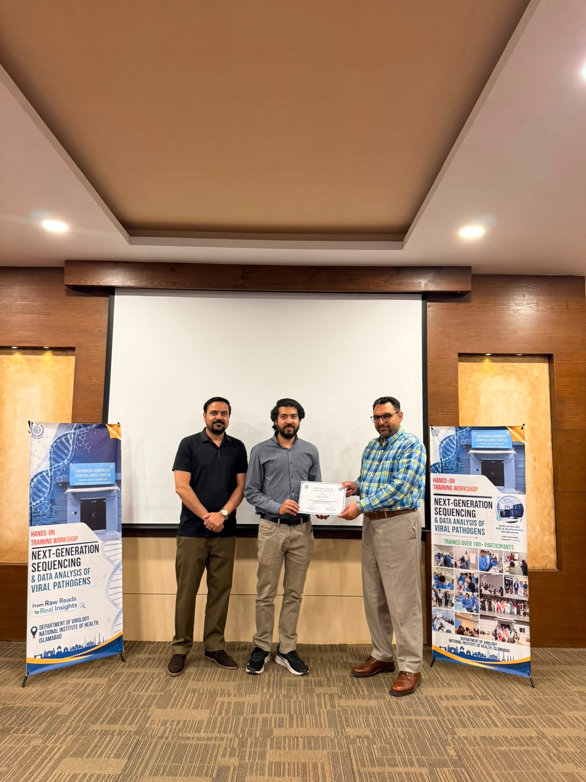 Syed Adnan Haider receiving recognition with colleagues after delivering hands-on NGS training at the National Institute of Health, Islamabad, in July 2026.